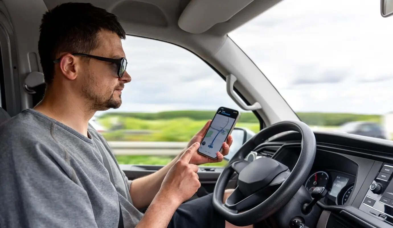 Hombre conductor usando GPS e interactuando con un smartphone; navegación en movimiento.